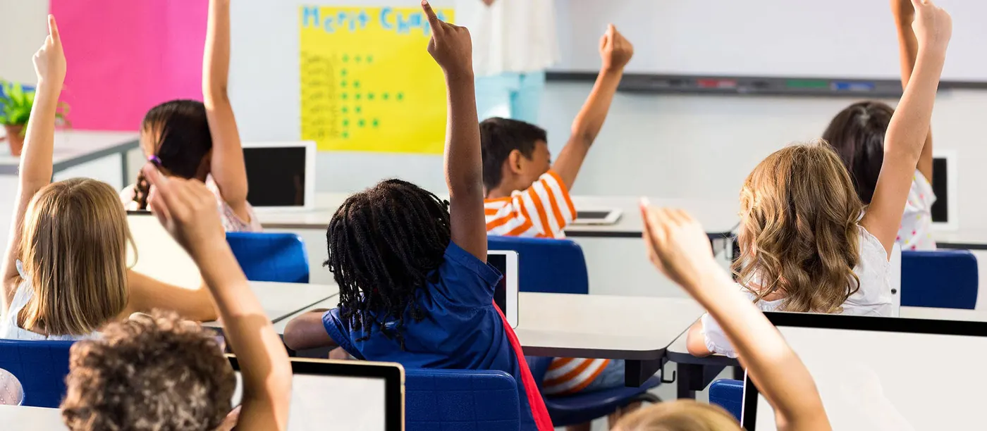 Alunos de braço no ar numa sala de aula